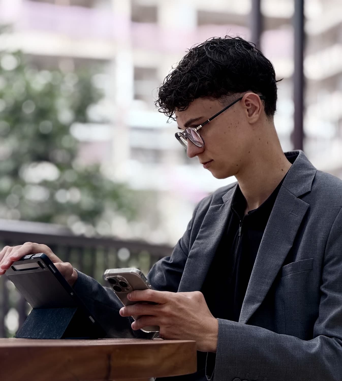 Arthur de perfil, à mesa ao ar livre, usando o celular ao lado de um tablet